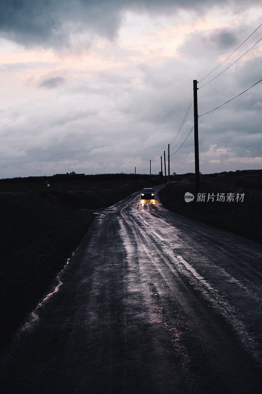 夜晚在远处的乡村道路上，汽车的前灯闪烁着