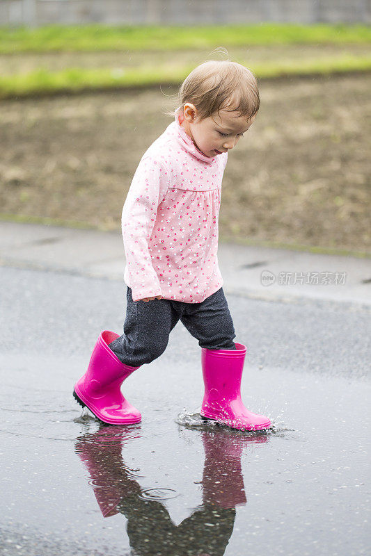 穿着雨靴的小女孩走过水坑