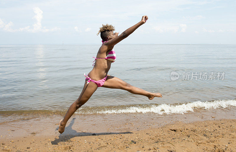 穿着比基尼的非裔美国女孩在海滩上跳跃