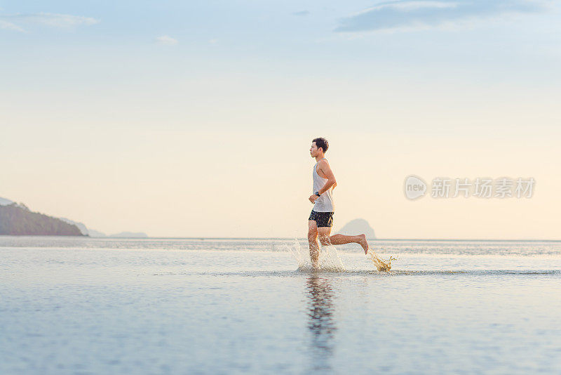 年轻的亚洲男子在海滩上奔跑，夕阳为背景