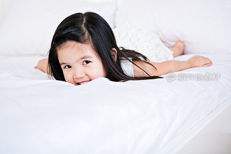 一个亚洲小女孩躺在床上。