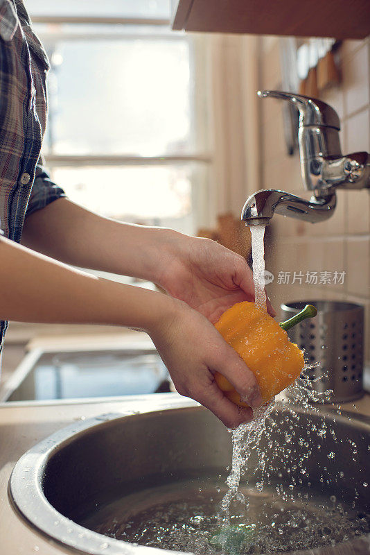 一个面目全非的女人在厨房里洗红辣椒。