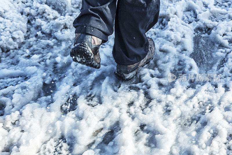 步行人的靴子踢起冬季城市人行道上的雪泥