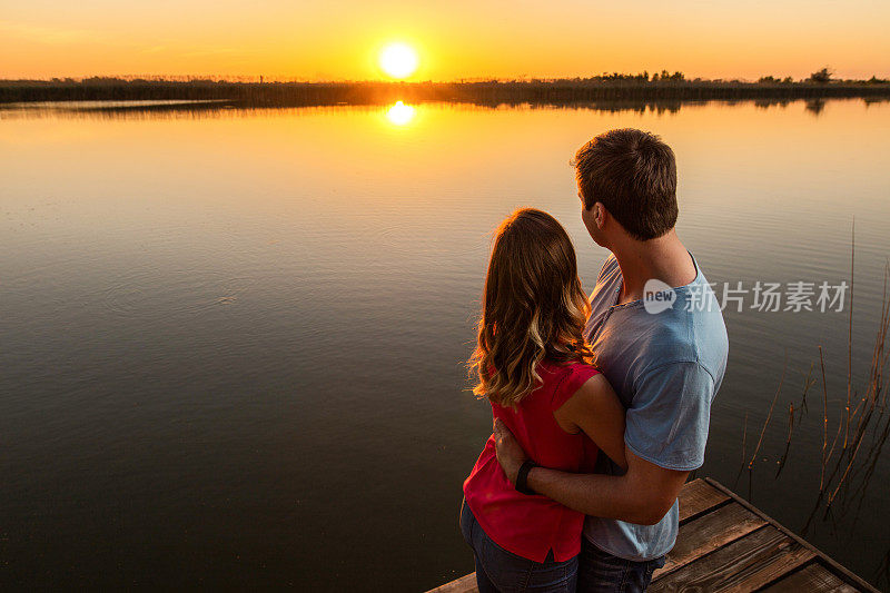 日落时码头上拥抱的夫妇的后视图。