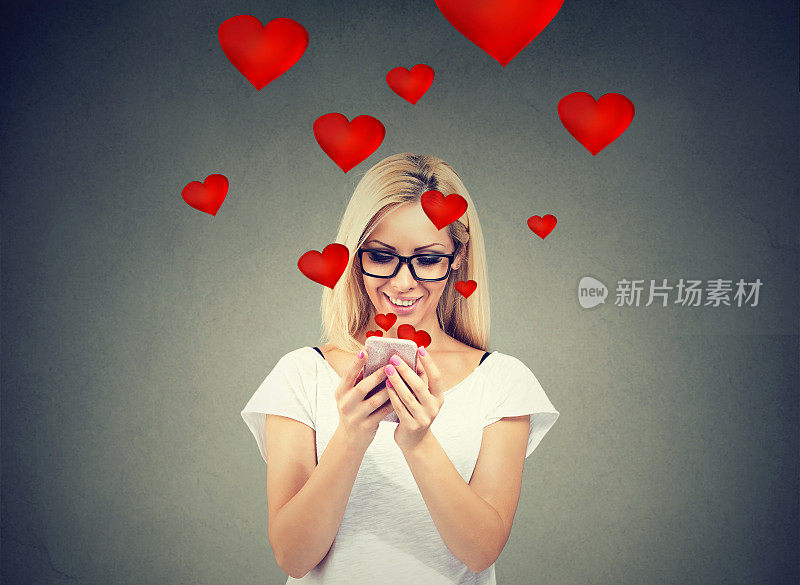 美丽的女人在手机发送爱的短信与红色的心飞离屏幕孤立在灰色的背景。