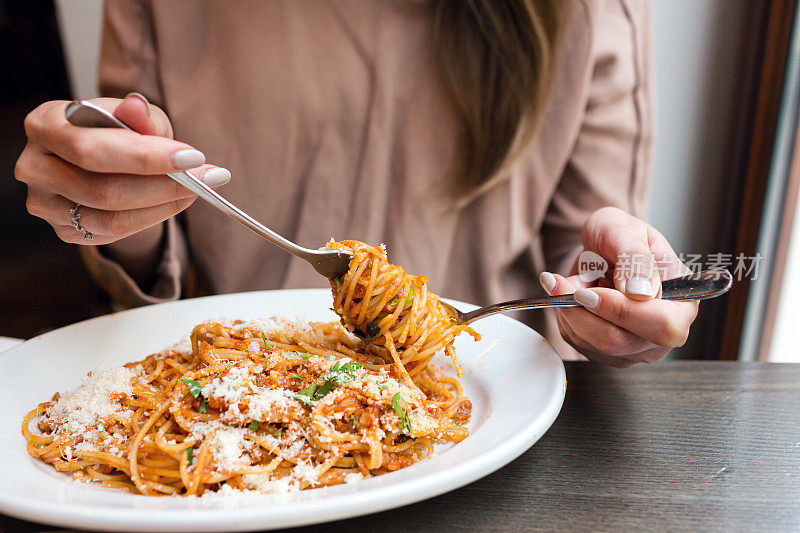 女孩吃意大利面加西红柿和肉。特写肉酱面，用勺子把它绕在叉子上。帕玛森芝士