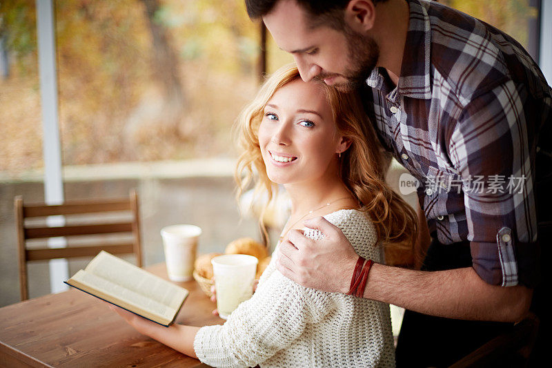 年轻女子读着一本书，男人拥抱着她