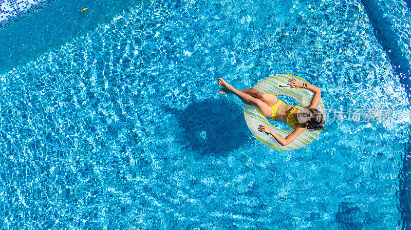 鸟瞰图的女孩在游泳池从上面，孩子游泳在充气圈甜甜圈和有乐趣的水在家庭度假