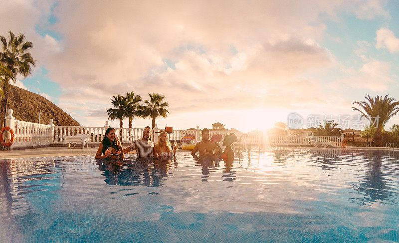 快乐的朋友喝香槟在游泳池聚会在日落-富有的人有乐趣在专属的热带度假-假日和友谊概念-主要集中在左边的家伙-原始的太阳颜色色调