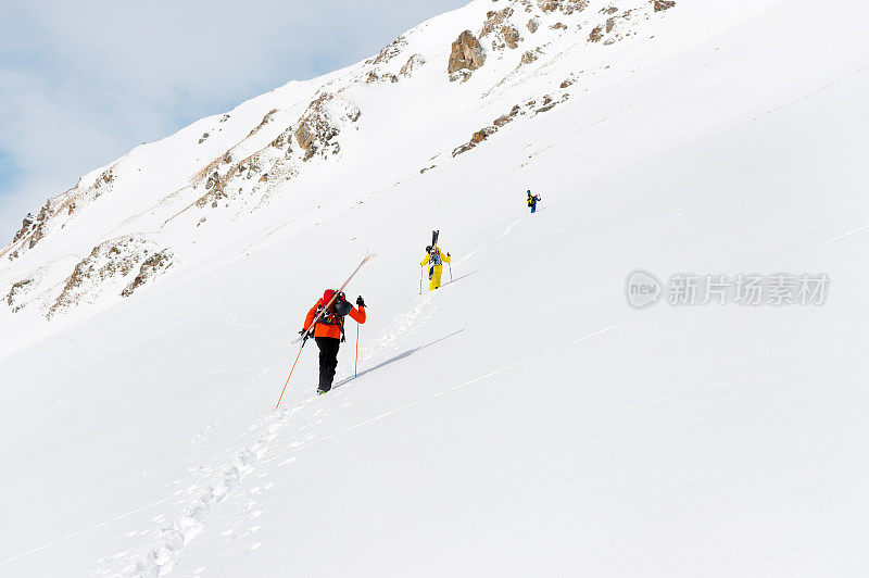 两个自由滑雪运动员爬上斜坡，背上的设备固定在背包上