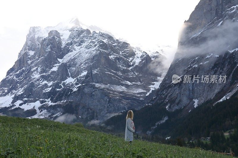 女人走进高耸的山脚下的草地