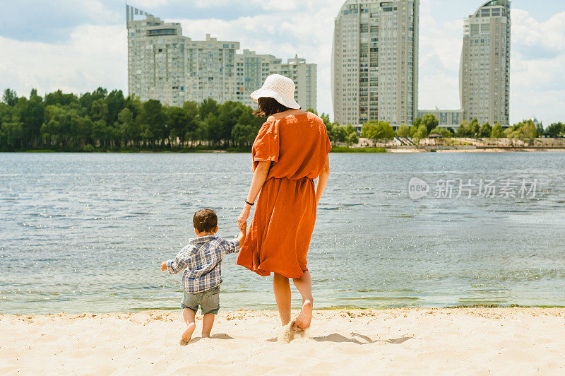 母子在沙滩上走到河边的背影