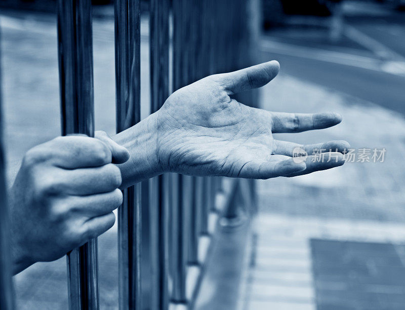 男人的手紧握着监狱的铁栏杆