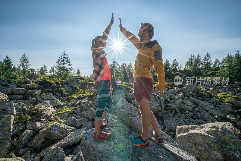 在山顶的一对夫妇站在岩石上，伸出双臂，代表自由和成功