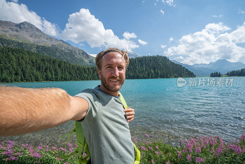 一个愉快的年轻人在一个美丽的山湖边自拍，享受一天的徒步旅行
