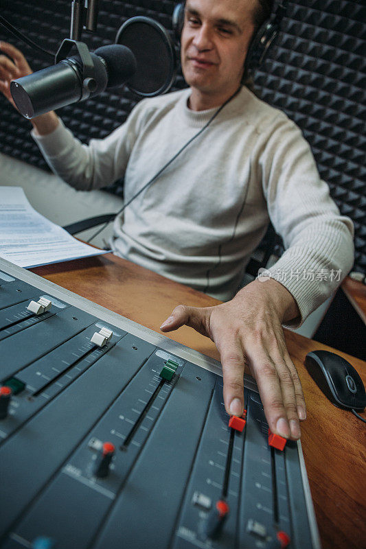 快乐微笑的男性电台主持人或主持人戴着耳机对着麦克风在电台讲话，肖像在工作场所