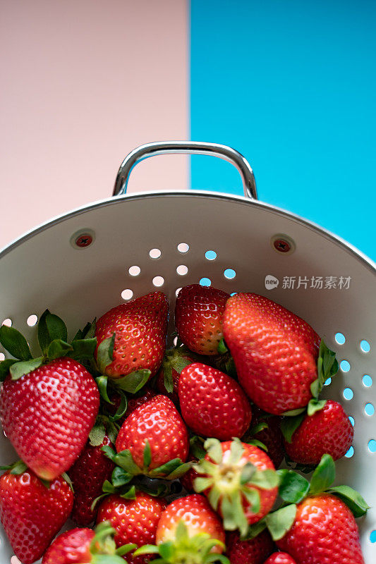成熟的草莓在一个古老的漏勺上，从上面的彩色背景