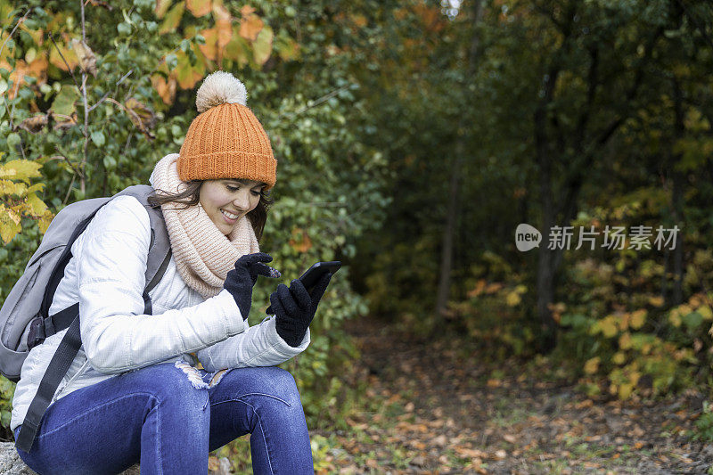 美丽的年轻女子看她的手机在森林在秋天