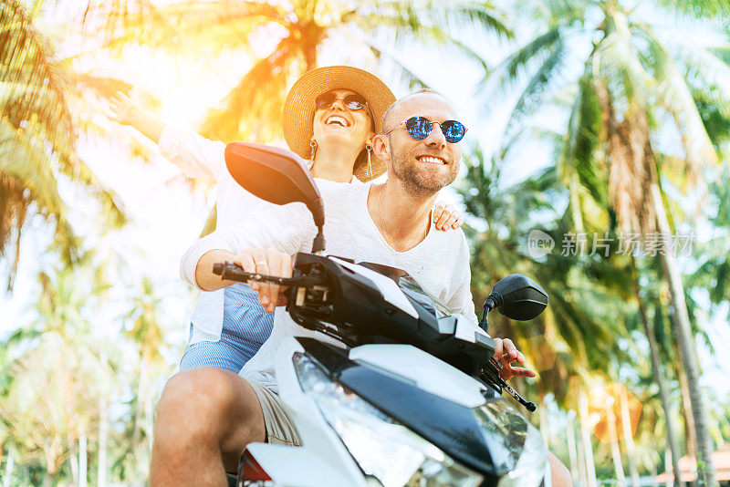 这对快乐的情侣在岛上度假时骑摩托车在棕榈树下