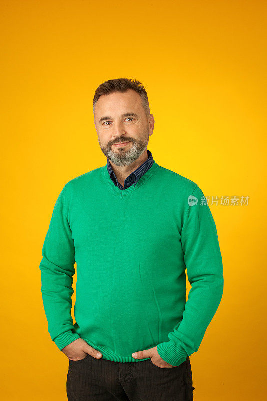 一个50岁的留着胡子的男人在黄色的背景上穿着一件绿色的毛衣
