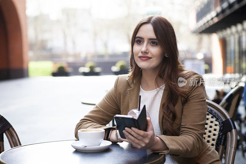 在咖啡馆外拿着咖啡和智能手机的女人
