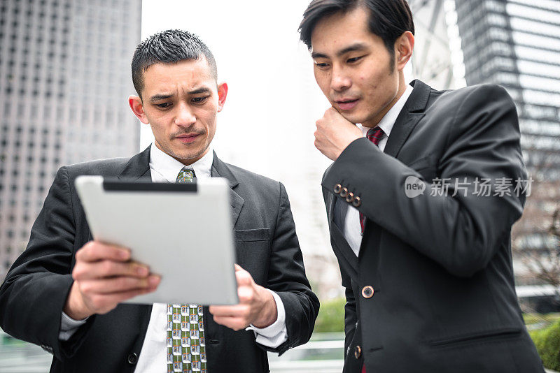 两个亚洲商人在平板电脑上读取数据