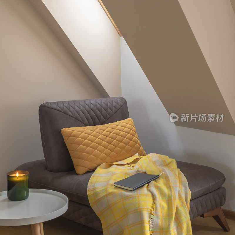窗边一个舒适的角落，沙发上有黄色的毯子和枕头，咖啡桌上放着蜡烛和书
