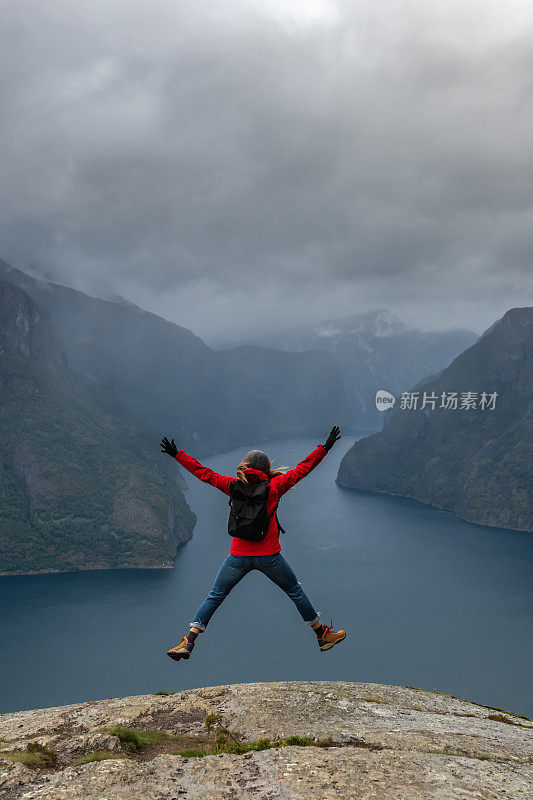 一个女人在峡湾边的山峰上跳。