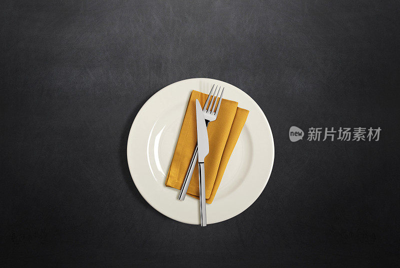 深色的餐桌上摆放着白色的盘子、刀叉和亚麻餐巾