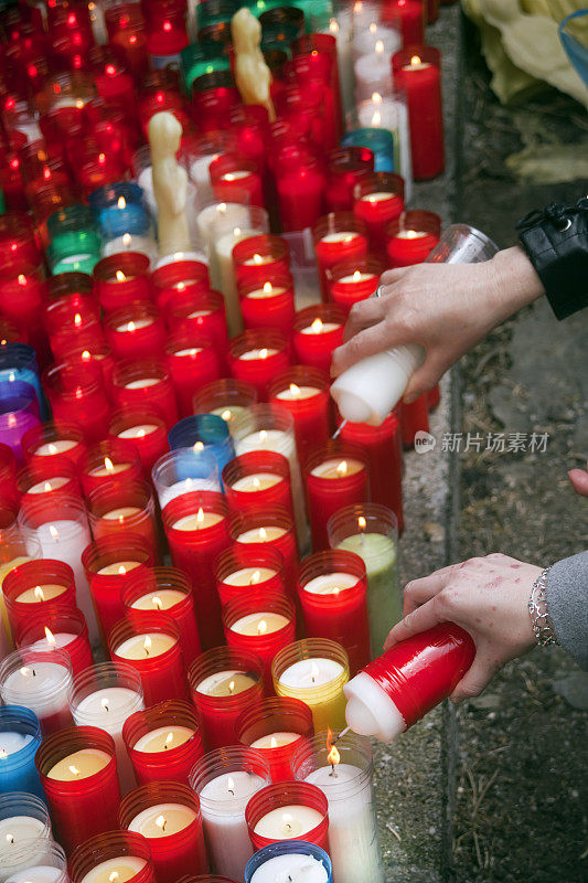 一组彩色的许愿蜡烛，女人的手牵着其中一根。
