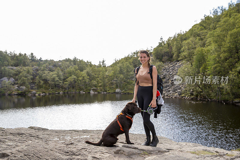 在挪威的布道石徒步旅行时，一位妇女正在训练她的拉布拉多猎犬