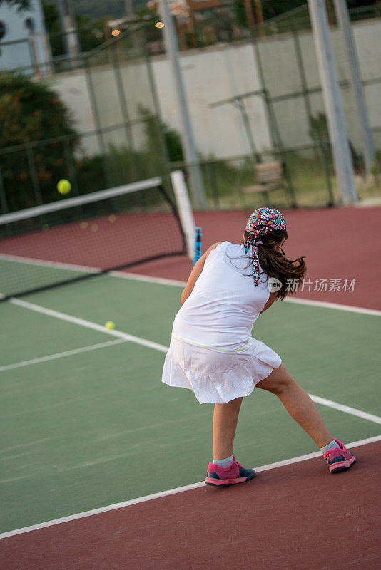 一个女孩和她的网球教练在硬地打网球，正手和反手投篮