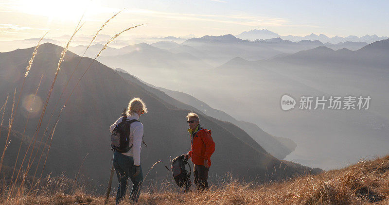 一对成熟的夫妇早晨沿着长满草的山坡徒步旅行