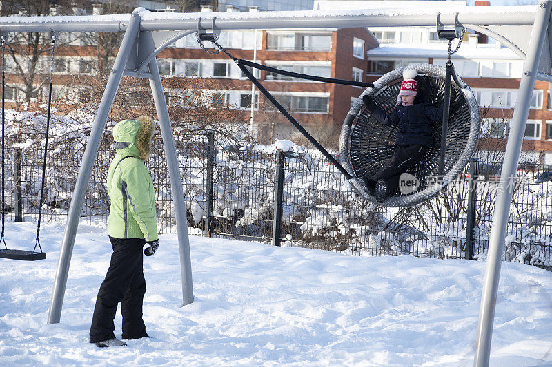 一位年轻的妇女和一个5岁的孩子在冬季城市公园的操场上散步。