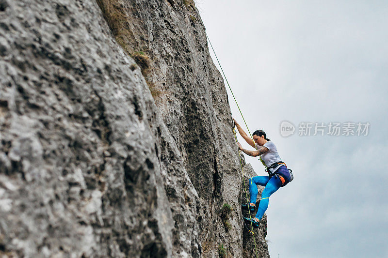 在她成功爬上悬崖顶端后，强壮的女性攀登者用绳子往下爬