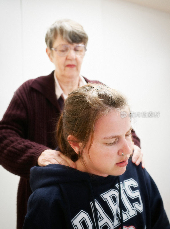 年长女性按摩年轻女性的颈部和头部，因为头痛，压力或肌肉痉挛