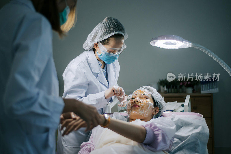 亚洲华人女性美容师在手术室手术前用棉球清洁她的客户的脸
