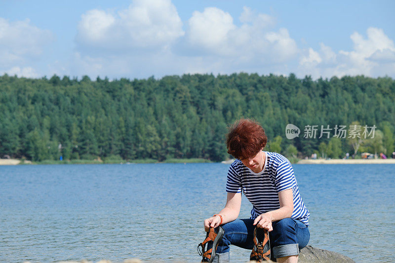 一个女人正在森林湖里洗她的脏脚和凉鞋