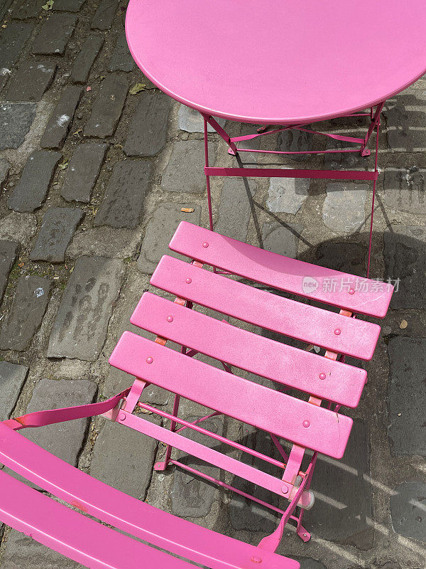 彩色的图像，圆形的金属庭院庭院桌椅漆成亮粉色，在鹅卵石街道上的露天餐厅，高架的视野