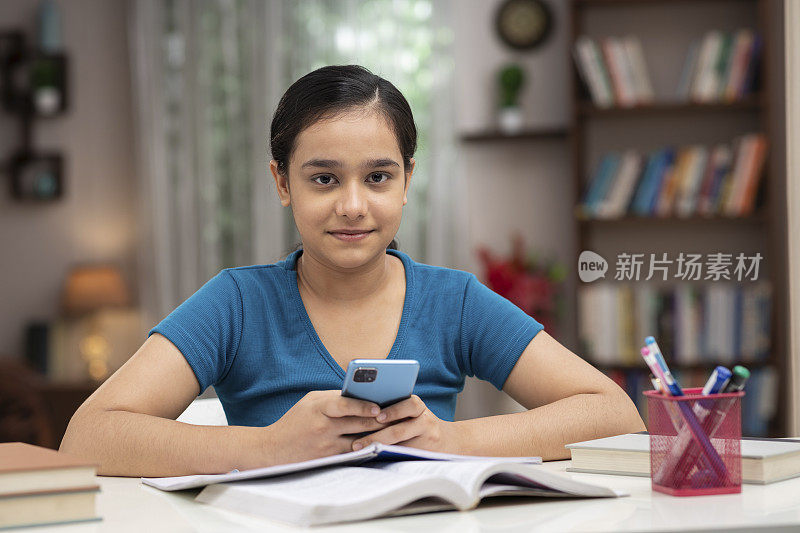 一个十几岁的女学生在家里用手机学习的照片:-库存照片