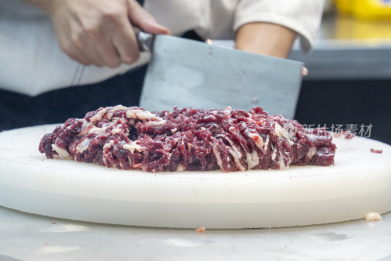 厨师在一家牛肉火锅餐厅的开放式厨房里用刀切牛肉