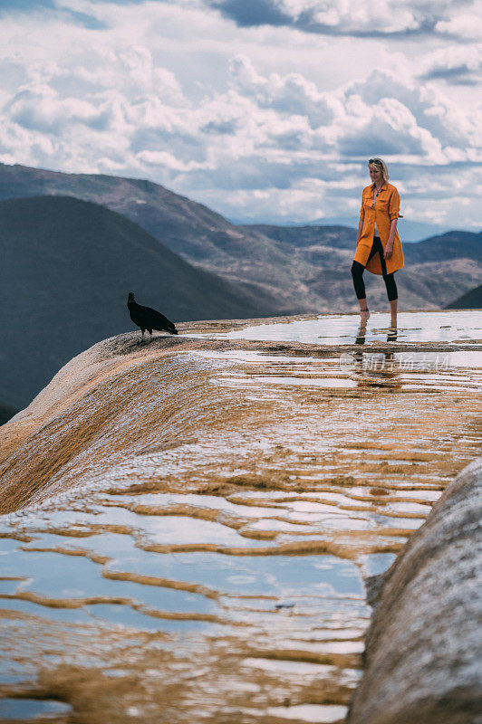 一个女人和一只黑秃鹫站在圣水山的边缘，俯瞰着壮丽的山景