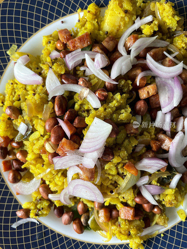 全框图像的蓝色镶边盘子的印度早餐食谱，poha(香料扁平米饭)菜洋葱，青辣椒，咖喱和香菜叶，花生，芥末和孜然种子，姜黄和柠檬汁，提高的观点