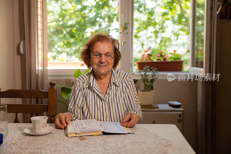 开朗的老年高加索妇女的肖像，94岁，坐在桌子和阅读一本书