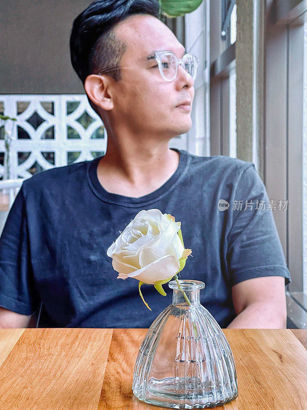 一名日本男子拿着玫瑰坐在餐桌旁。