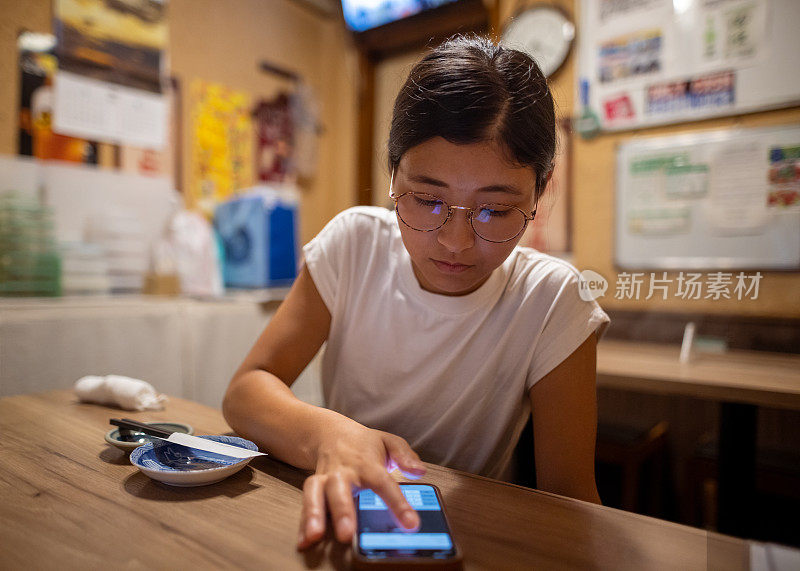 一名年轻女子在日本“居酒屋”用智能手机等待上菜