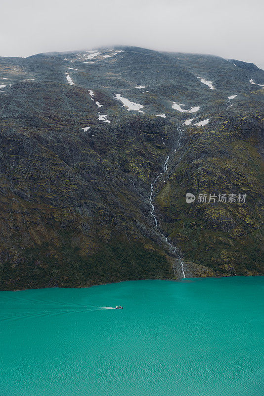 在挪威约顿海门国家公园水晶蓝色的冰川湖上航行的渡轮的戏剧性视图