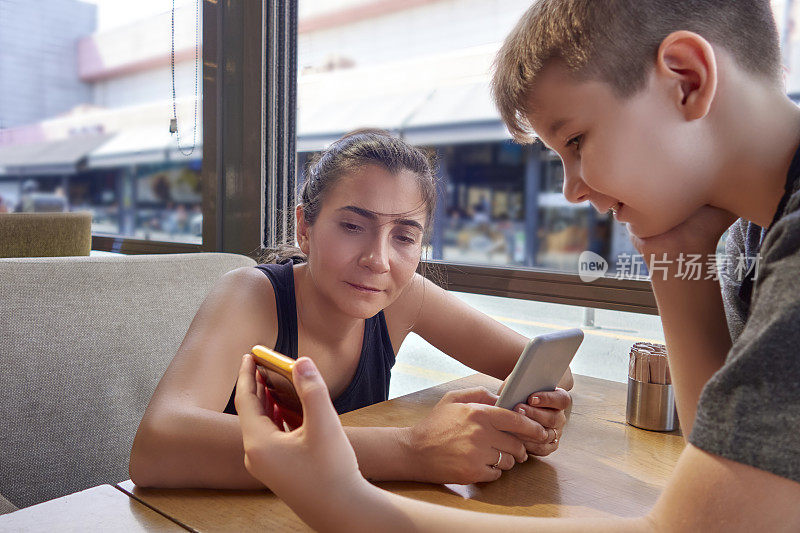 母亲和儿子在餐厅吃午饭时使用智能手机