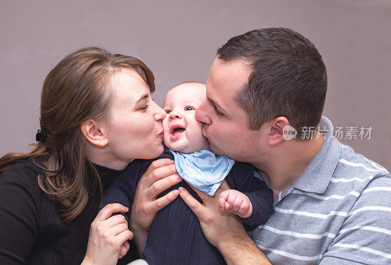 一个年轻的白人家庭的肖像，一个年轻的男人和女人拥抱和亲吻一个小婴儿