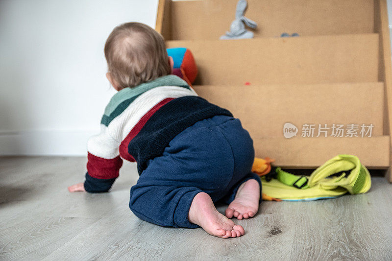 一个婴儿在家里的架子上捡玩具的后视图